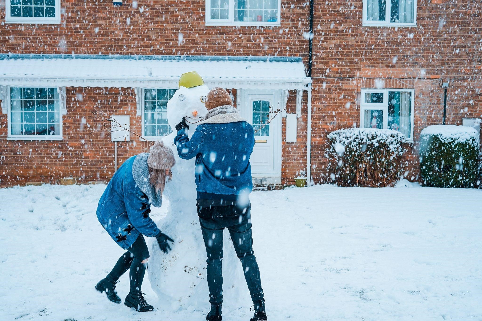 A young couple playing with snow outside their home on cold